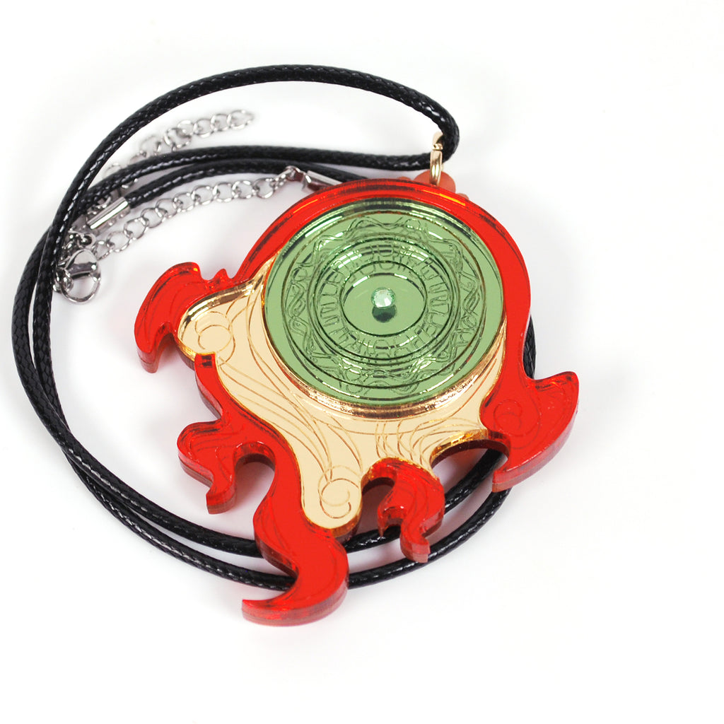 A fanartist creation of the Okami divine retribution disk, featuring gold, red, and green mirror acrylics with a green rhinestone in the middle on a black cord necklace.