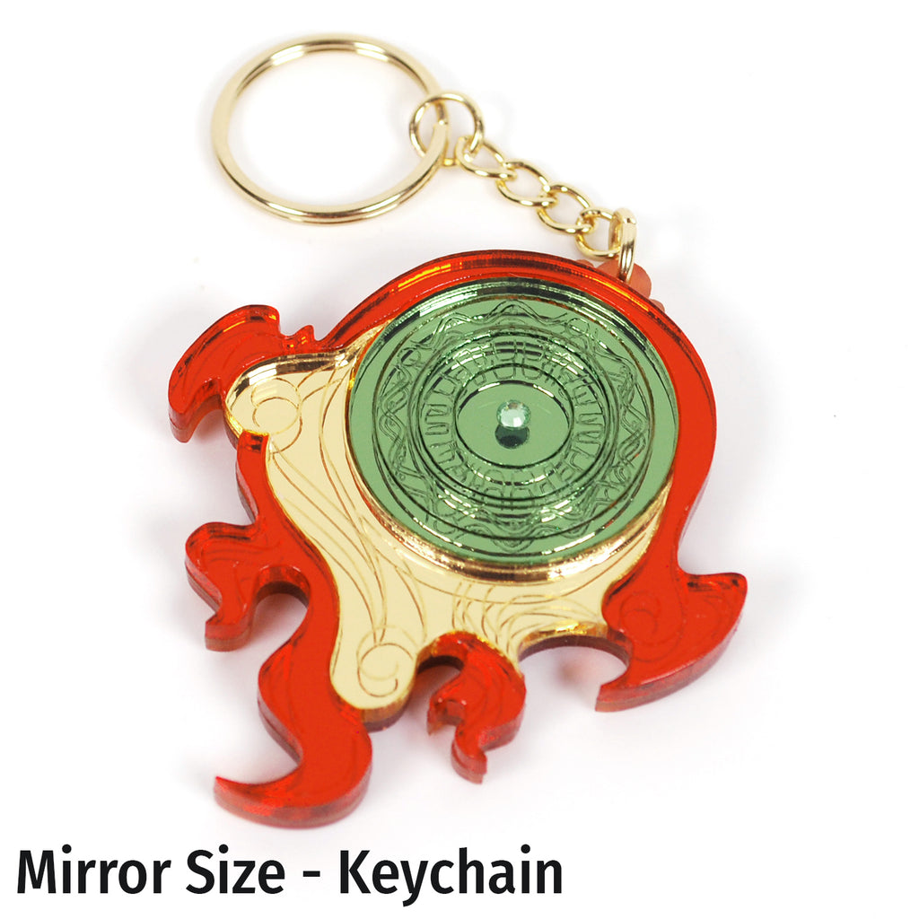 A fanartist creation of the Okami divine retribution disk, featuring gold, red, and green mirror acrylics with a green rhinestone in the middle on a gold dangle keychain.