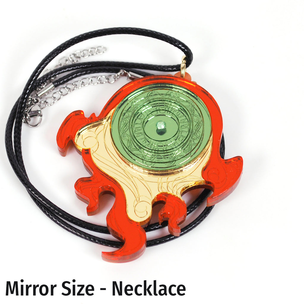 A fanartist creation of the Okami divine retribution disk, featuring gold, red, and green mirror acrylics with a green rhinestone in the middle on a black cord necklace.
